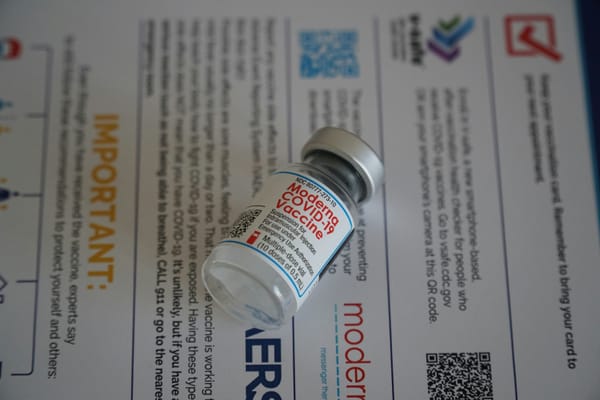 A vial labeled "Moderna COVID-19 Vaccine" on its side atop an information sheet.