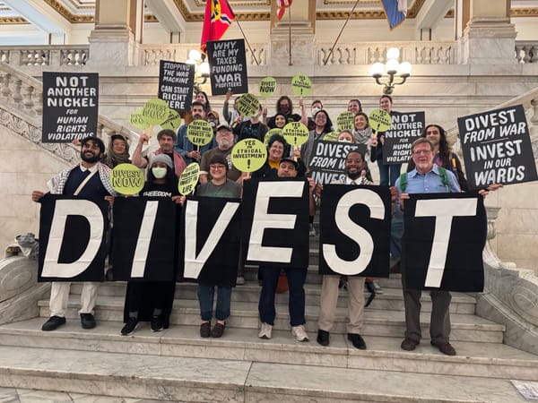 About two dozen people on marble steps with green, black, and white signs calling for divestment from war and human rights violations. Th front row hold large signs spelling "DIVEST."