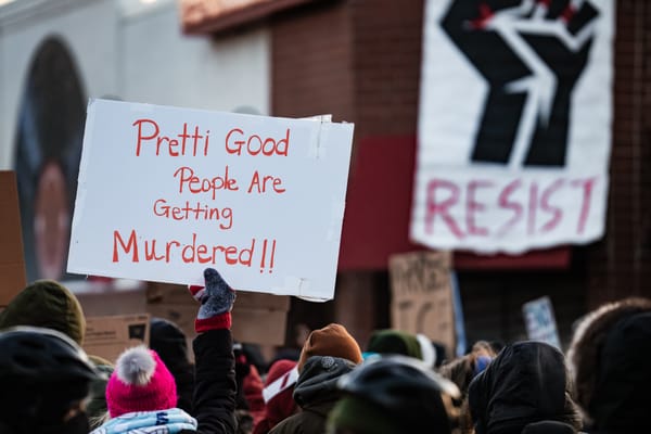 Tops of heads of people marching. Two signs are visible: One with a black fist reads "RESIST" in red. Another with red letters on white reads "Pretti Good People Are Getting Murdered!!"