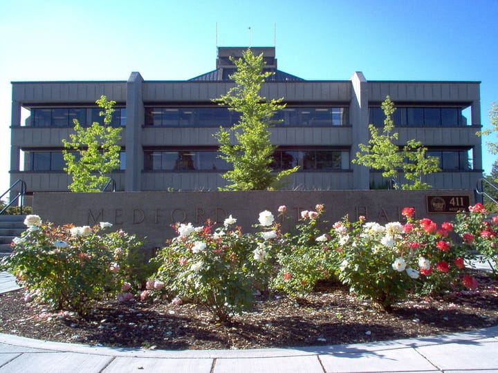 A brown three-story building with a small rose garden in front.