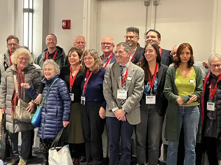 A group of about fifteen people wearing conference lanyards post smiling in front of a double door.