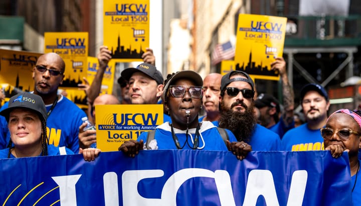 A crowd of people wearing blue march with yellow UFCW Local 1500 signs and a large banner.