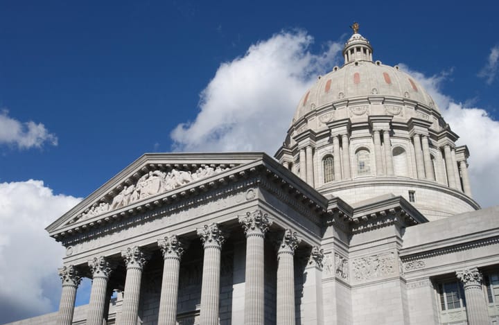 A Baroque dome and columned facade photographed against a blue sky with a couple of fluffy white clouds.